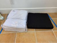 Curtain panels and seat cushion shown side-by-side on tiled floor, curtain panels wrapped in plastic packaging.