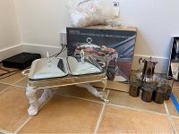 Showing silver plated 2-in-1 chafing dish with hinged lids and beverage set including a pitcher and four glass tumblers with holders on a tiled floor.