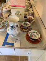 Photo showing Royal Tara Irish Fine Bone China vase, three tea cups, and three saucers with floral patterns and original packaging box in background.