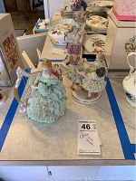 Three Irish Dresden porcelain figurines displayed together on a table with tagging label. Includes two women figurines and one with harp, showing overall condition and size relative to surrounding dishware.