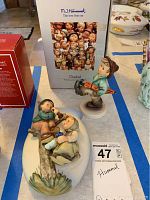 Photo of two M.J. Hummel figurines, the plaque and the boy figurine with original box in background