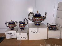 Full view of the teapot, creamer, sugar bowl, and one tea cup with saucer on boxes