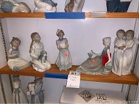 Shelf holding 5 porcelain Lladro figurines of children and animals.