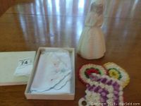Lladro figurine next to knitted coasters and boxed linen bun wrap on wooden table