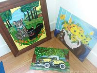 Photo of three 20x24 framed paintings shown leaning against walls on floor, including a cat painting, floral painting, and vintage yellow car painting