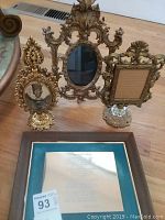 Three gold-tone decorative pedestal picture frames and an award plaque on wooden floor.
