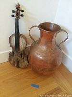 Metal vat and decorative violin side by side in a corner on wooden floor