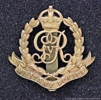 Front side of the Royal Military Police WW1 cap badge showing detailed design of crown, cypher and laurel wreath on textured black background.