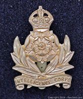 Front view of the WW2 Intelligence Corps cap badge showing the crown, rose emblem, laurel leaves, and Intelligence Corps banner.