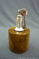 Front-right side view of the table lighter, showing wooden base and metal lighter top.