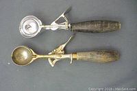 Top view of two vintage ice cream scoops, Clipper (silver metal) and Tudhope (brass/bronze metal) with wooden handles