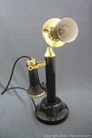 Full view of the vintage lamp shaped like an antique candlestick telephone in black and brass colors, showing the earpiece and stand.
