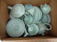 Full view from above of boxed lot showing ceramic teapots, cups, saucers, and plates in pale green glaze with Art Deco ribbed detailing.