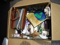 Top view of a cardboard box containing assorted items including handbags, a book, a white cup with a nautical design, a black umbrella, and various small household articles.