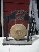Front view of small metal gong on black wooden stand with decorative circular cutout design.
