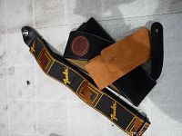 Three guitar straps laid on a white surface: Fender branded strap black with yellow logos and gold patterns, plain brown strap with snap button, black strap with brown Levi's leather patch.