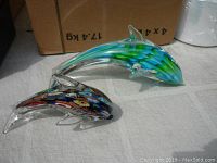 Pair of glass dolphin figurines on light background with cardboard box in view