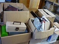 Shows large cardboard boxes filled with assorted decorative and houseware items including a beige toolbox and green container.