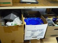 Box with various decorative and houseware items including a bright blue plate and assorted metalware.