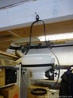 Full view of antique hanging lantern with white glass shade in wrought iron frame, hanging inside a room with wooden ceiling.