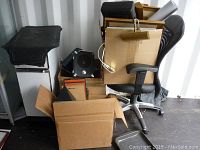 Overview of lot showing office chair, cardboard boxes with frames, speaker, lamp, and compactor