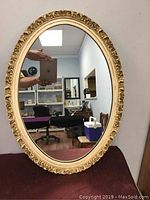Front view of vintage oval mirror showing ornate gold frame with leaf and scroll detailing, measuring 25.5 by 18.5 inches.