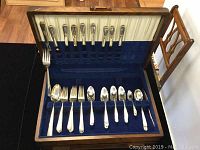 Full wooden box with blue velvet and white satin lining showing one layer of silver plated cutlery arranged meeting service for six plus extras.