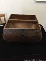 Side view of the antique Asian wooden basket showing the curved body, wooden stitching, and metal studs on the corners.
