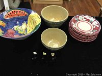 Overall view of entire lot on black cloth, showing large colorful Italian bowl, plates stacked, two mixing bowls and pie birds in front
