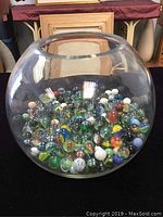 Front view of large clear glass fishbowl filled with assorted vintage marbles of various colors.