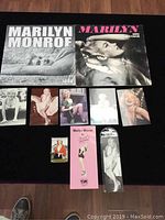 Full layout of Marilyn Monroe memorabilia including both calendars, an array of postcards, bookmarks, and display items on black surface.