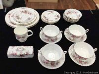 Full view of the set including plates stacked by type, double-handled cups on saucers, the mug, butter dish cover, and extra saucers arranged on black fabric.