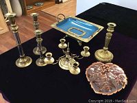 Full view of all brass ware items including candlesticks, candelabra, blue enamel tray with gold detail, and copper leaf dish on black surface.