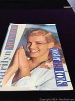 Cover of the Marilyn Monroe poster book, showing Marilyn smiling with hands together