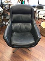 Front view of the vintage modern black faux leather lounge chair showing curved armrests, cushioned segmented backrest, and wear on seat cushion.
