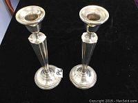 Two silver candlesticks standing upright on black surface showing overall shape and details.