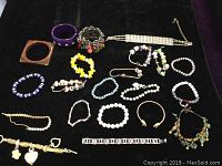 Photo showing assortment of bracelets and one necklace on black surface, varying colors and materials present.
