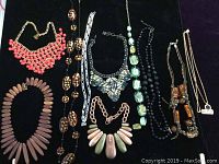 Lot of 10 assorted costume jewelry necklaces arranged on a dark surface with varied styles and materials.