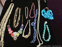 Full view of all 9 different costume jewelry necklaces arranged on black background.
