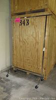 Full front view of large metal coat rack on wheels with plywood backdrop and pink sticker on horizontal bar