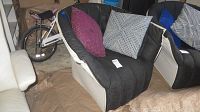 Front angle of Ligne Roset chair showing white leather arms and base with black canvas seating. Three pillows included: red geometric, black and white striped, and blue.