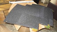 Group of black carpet tiles laid out on a table showing texture and size.