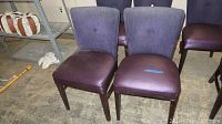 Four plum-colored dining chairs with fabric backs and satin-like seats arranged in a row, showing two chairs fully and two partially behind