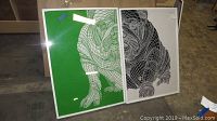 Two framed wall art prints of bulldogs leaning against a wall on a warehouse floor.