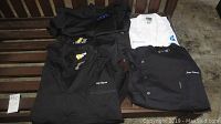 Six chef jackets laid out on table, mostly black with one white, all embroidered with 'Jose Garces'
