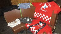 Multiple chef aprons and jackets including red Japanese style jackets and white, grey, blue shirts laid out on a curved bench.