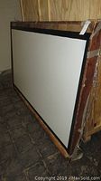 Front angle showing the white screen surface with black border mounted firmly on a wooden crate.