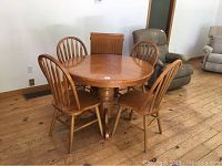 View of the round oak dining table with four matching chairs arranged around it on a hardwood floor.