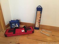 Overview photo showing blue cooler bag, red croquet bag, croquet mallets in blue bag, and metal horseshoes on wooden floor near corner wall.