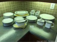 Overall view of stacked dinner plates, salad plates, small plates, bowls, cups, saucers, platters, gravy boat, creamer, and sugar bowl displayed on countertop